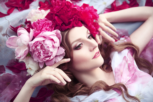 woman in a wreath of peonies lies among petals - Zdjęcie, obraz