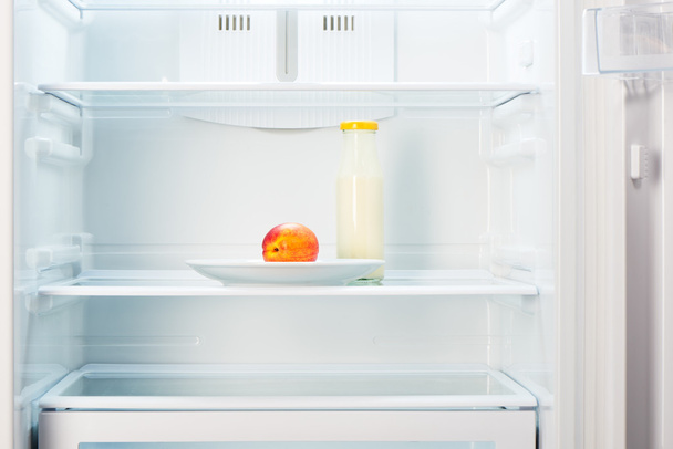 Peach on white plate with bottle of yogurt in refrigerator - Photo, Image