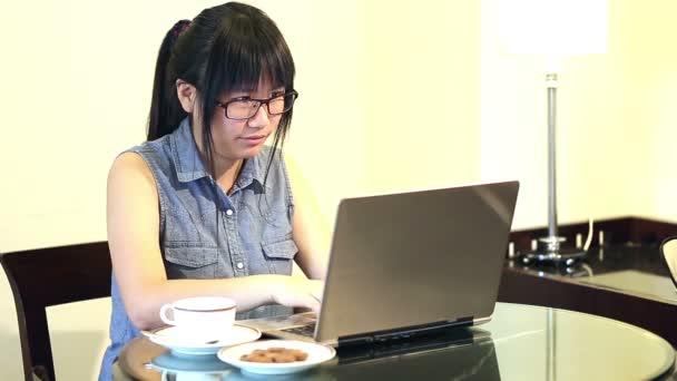 Ασιατικές γυναίκα φοράει γυαλιά που κάθεται στην καρέκλα στο σπίτι και εργάζεται σε ένα φορητό υπολογιστή - Πλάνα, βίντεο