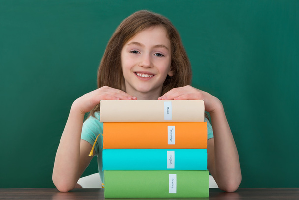 Girl Sitting At Desk With Stack Of Books - Foto, immagini