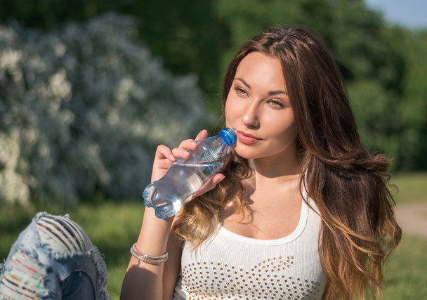 Mooi meisje in een wit overhemd is drinkbaar water uit een fles - Foto, afbeelding