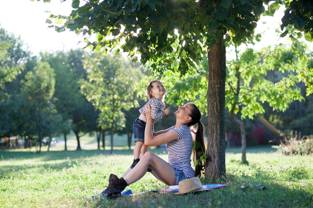 Mother and toddler sitting under the tree during summer  vacation - Photo, Image