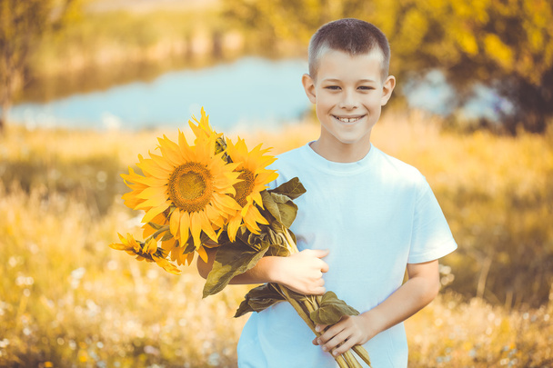 Ευτυχισμένο αγόρι με μπουκέτο από ηλιοτρόπια κατά πεδίο καλοκαίρι - Φωτογραφία, εικόνα