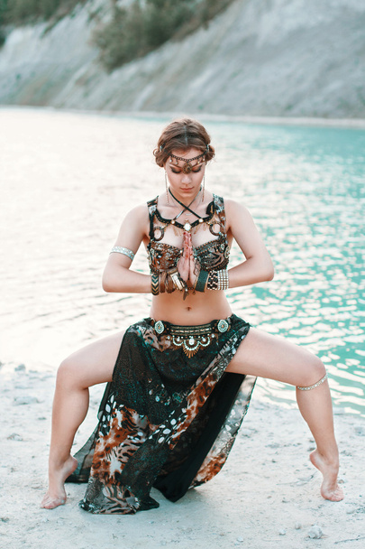 Hermosa chica en traje de fusión tribal de pie en una pose a orillas de la playa, fondo de mar azul
. - Foto, Imagen
