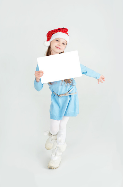 Cute girl in Santa Claus hat with a white blank paper sheet. - Фото, зображення