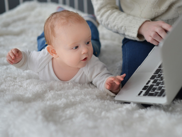 Woman with baby and laptop sitting on bed at home - Foto, Imagen