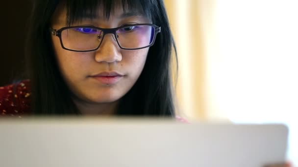 Ασιατικές γυναίκα φοράει γυαλιά κάθεται σε ένα κρεβάτι στο σπίτι και να εργάζεται σε ένα φορητό υπολογιστή - Πλάνα, βίντεο