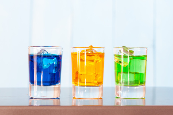 Three kinds of alcoholic drinks in shot glasses on bar counter and light background - 写真・画像