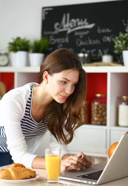Attractive young woman using laptop and sitting in the kitchen  - Foto, Imagen