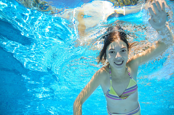Child swims in pool underwater, happy active girl has fun in water, kid sport on family vacation - 写真・画像