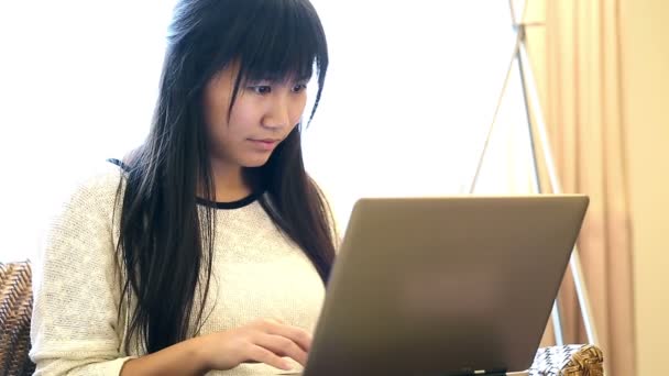 Aziatische vrouw zit op stoel thuis en ze werken op een laptop - Video