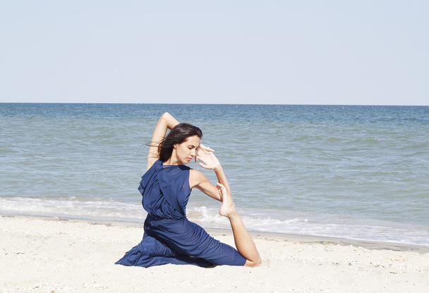 Young beautiful woman doing yoga at seaside in blue dress - Фото, зображення