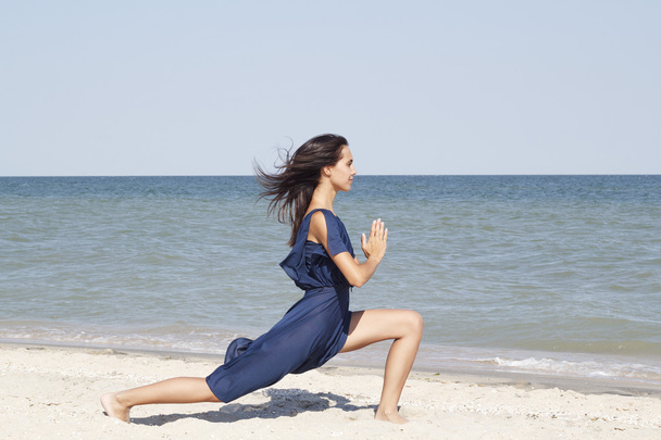 Young beautiful woman doing yoga at seaside in blue dress - Photo, Image