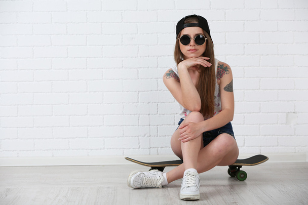 Beautiful hipster girl with skateboard on light background - Foto, Imagem