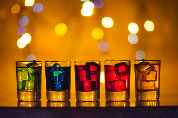 Öt lövés pohár tele válogatott italokat és jeges arany homályos világítás bokeh háttér - Fotó, kép