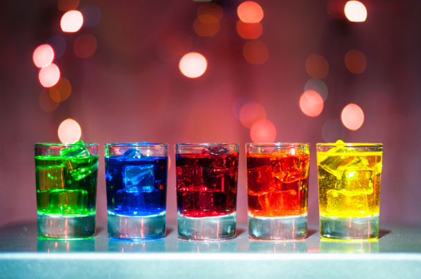 Five shots glasses full of assorted beverages and ice on golden blurred lighting bokeh background - Photo, Image
