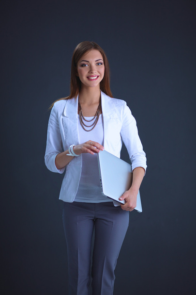 Young woman holding a laptop, standing on gray background - 写真・画像