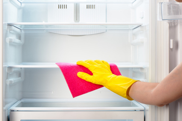 Woman's hand in yellow glove cleaning refrigerator with pink rag - 写真・画像