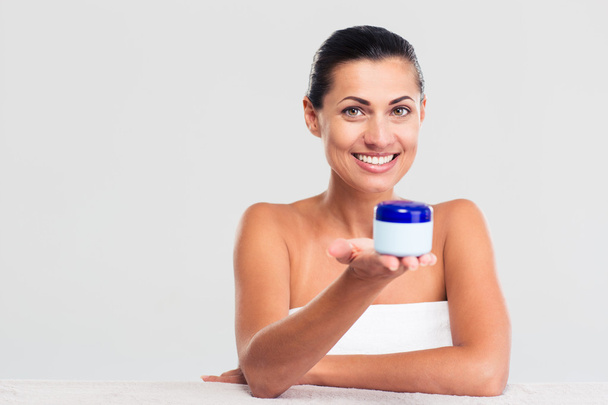 Woman in towel sitting at the table and holding cream jar - Foto, Imagen
