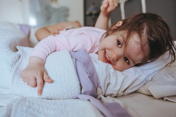 Μικρό κορίτσι χαμογελά που βρίσκεται πάνω από το κρεβάτι - Φωτογραφία, εικόνα