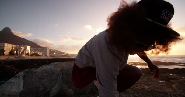 Menina afro de pé sobre pedras na praia
 - Filmagem, Vídeo