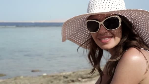 mooie vrouw in een hoed en zonnebril zonnebaden op het strand - Video