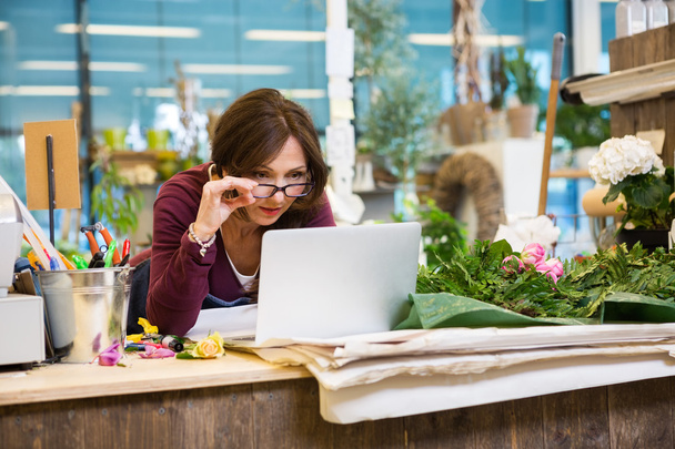 Florist Holding Glasses While Using Laptop In Flower Shop - Photo, image