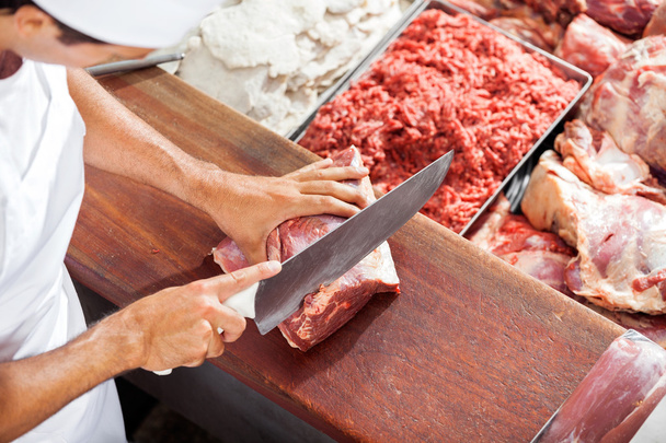 Smiling Butcher Cutting Meat At Counter - Foto, imagen