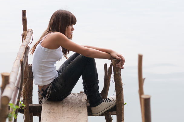vrij tienermeisje zittend op het dok naast de rivier op mooie zomerdag - Foto, afbeelding