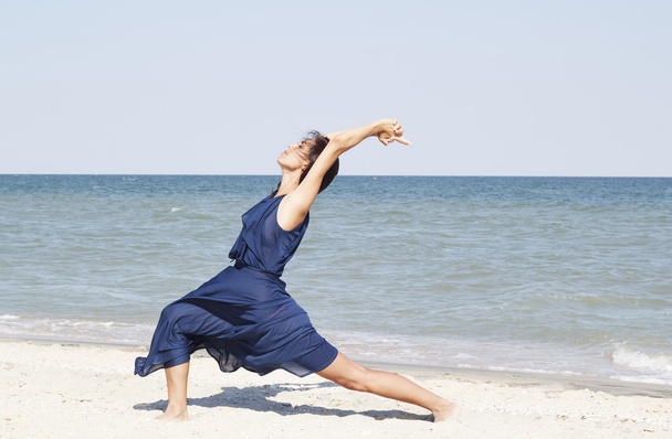 Young beautiful woman doing yoga at seaside in blue dress - Foto, Imagen
