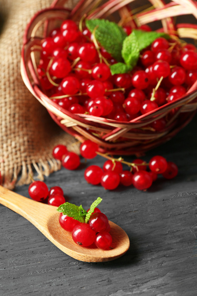 Ripe red currant in wicker basket on wooden background - Foto, afbeelding