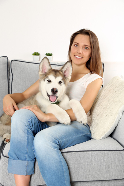 Woman sitting with her malamute dog on sofa in room - Foto, Bild