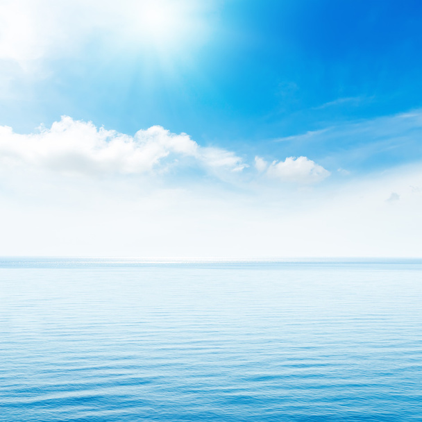 zon in blauwe wolken boven zee - Foto, afbeelding