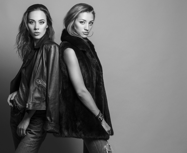 Fashion shot of two elegant beautiful girls (brunette and blonde) in studio on grey background, dressed in casual clothes . Shopping inspiration. Monochrome (black and white)  photo - Fotó, kép