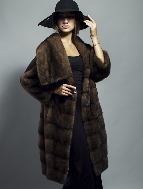 Sexy Beauty Girl with natural  Make up.  Fashion Blonde Portrait of a girl dressed in fur coat and black hat posing on a grey background. Retro style - Фото, зображення