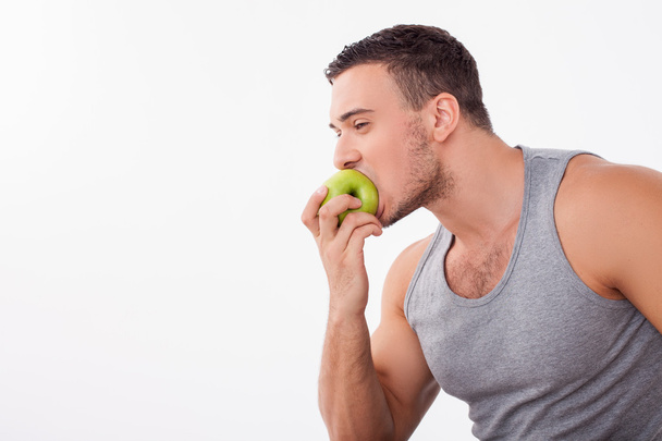 Cheerful young guy is biting a fruit greedily - Zdjęcie, obraz