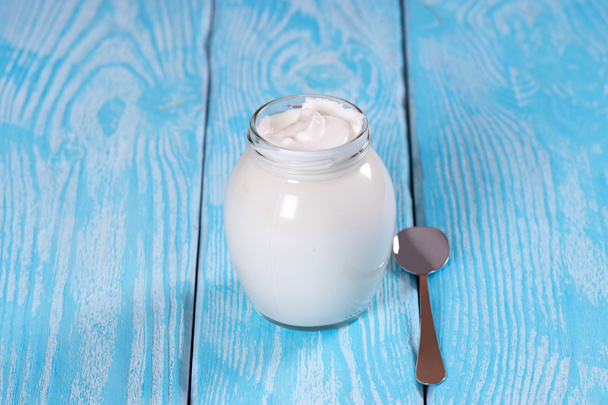 Bulgarian yogurt in a jar with a spoon. Blue background. - Foto, afbeelding