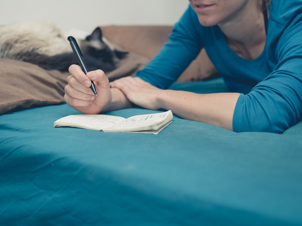Woman taking notes in bed with cat - 写真・画像