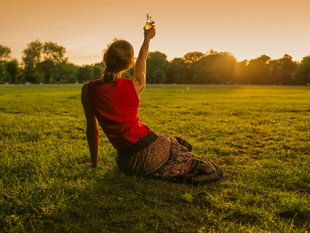 Vrouw opheffing fles tot zonsondergang in park - Foto, afbeelding
