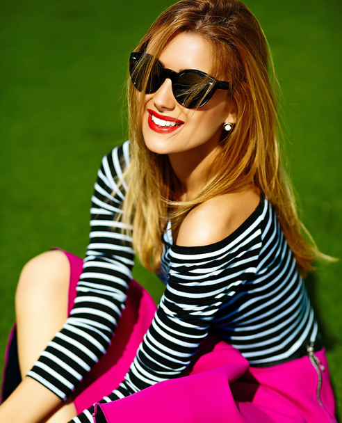 Funny crazy glamor stylish sexy smiling beautiful blond young woman model in pink hipster clothes sitting in the grass in the park - Photo, image
