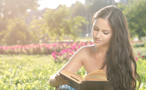 young brunette reading a book in the park - Fotó, kép