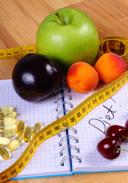 Fruits, tablets supplements and centimeter with notebook, slimming and healthy food - Photo, Image