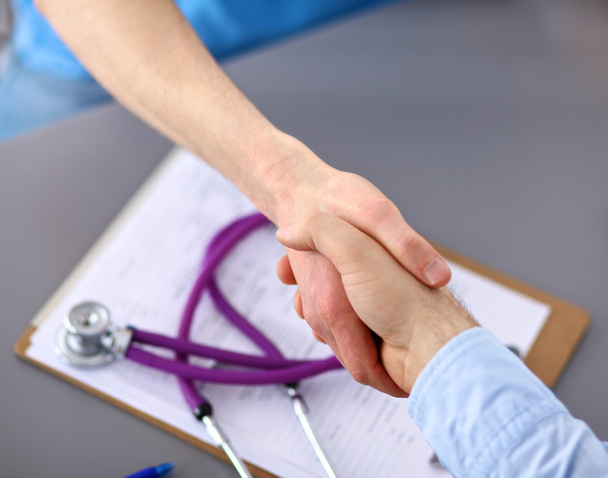 Atractiva doctora dándole la mano a un paciente en su consultorio
 - Foto, Imagen