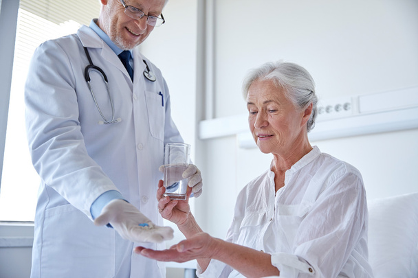 arts geeft geneeskunde aan oudere vrouw in het ziekenhuis - Foto, afbeelding