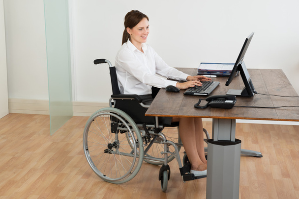 Businesswoman On Wheelchair While Working On Computer - Foto, Bild