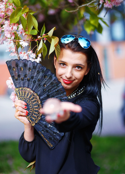 Young woman smelling a beautiful sakura blossom, purple flowers. Spring Magic, Magical Glass sphere in hand and beautiful ornamental fan - Fotografie, Obrázek