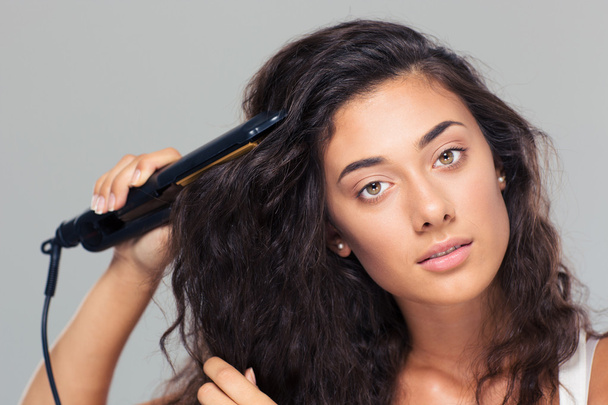 Woman doing hairstyle with hair straightener  - Zdjęcie, obraz
