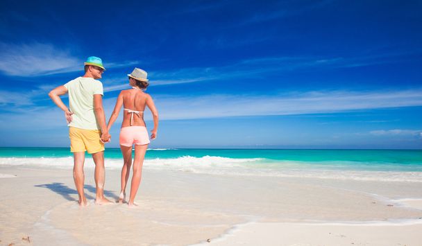 Vista trasera de pareja con ropa brillante cogida de la mano en la playa tropical
 - Foto, Imagen