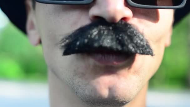Um homem de chapéu e bigode grimaces
 - Filmagem, Vídeo