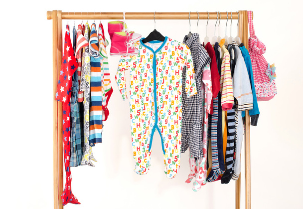 Dressing closet with clothes arranged on hangers.Colorful wardrobe of newborn,kids, toddlers, babies full of all clothes.Many t-shirts,pants, shirts,blouses,yellow hat,shoes, onesie hanging - Photo, image